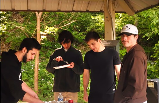 Four members plating food together under a park shelter